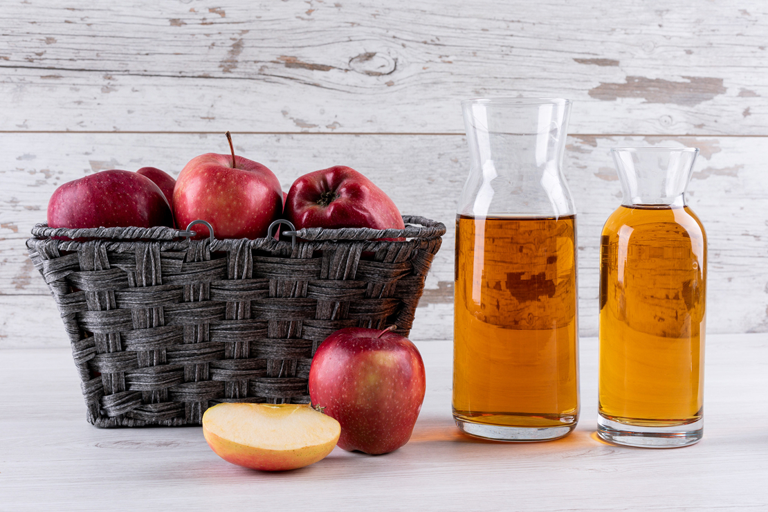 A bottle of apple cider vinegar with fresh apples and measuring tape