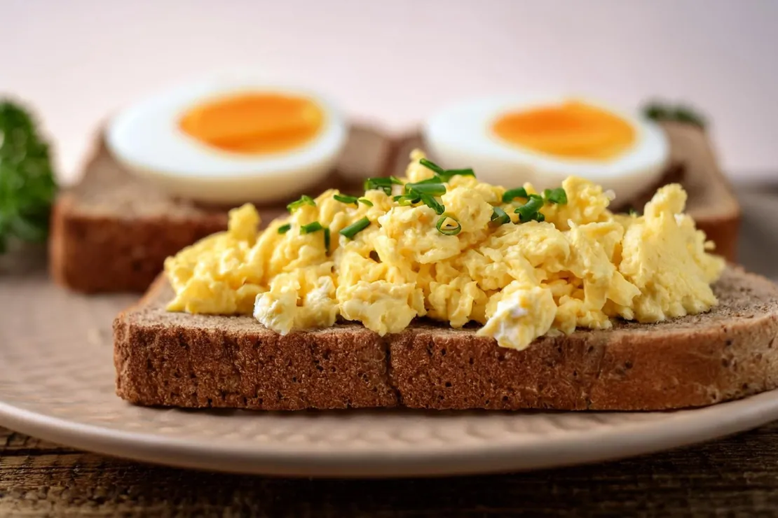 A plate with a slice of bread topped with scrambled eggs and another with a boiled egg, illustrating the comparison.