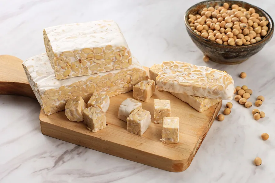 Blocks of tempeh on a wooden cutting board with soybeans, highlighting its fermented texture.