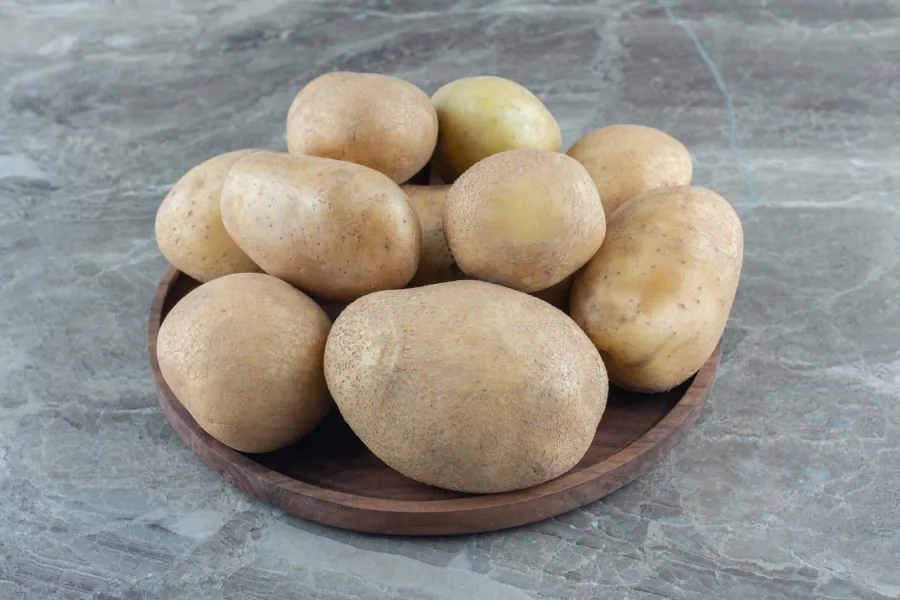 A small pile of red-skinned regular potatoes on a light wooden surface
