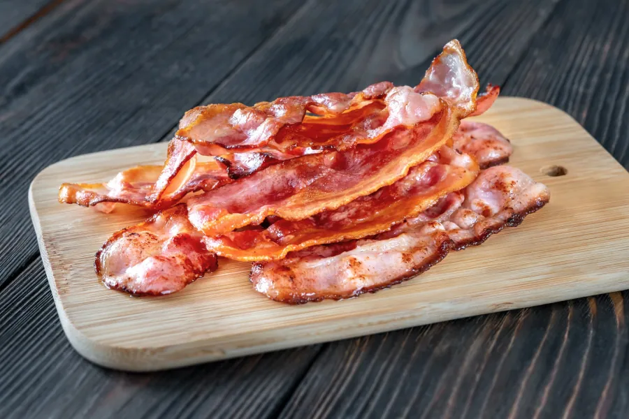 A stack of crispy traditional pork bacon strips on a small wooden cutting board